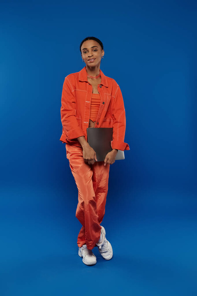 A woman in an orange jumpsuit holding a laptop. - Photo, Image
