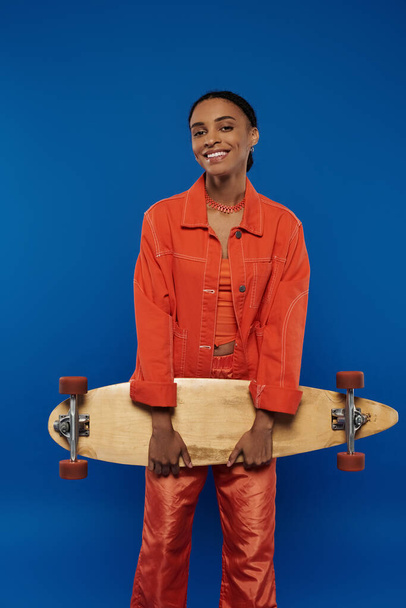 Une femme en chemise orange tient un skateboard en toute confiance. - Photo, image