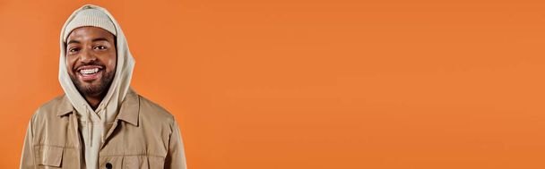 Ένας κομψός Αφροαμερικάνος με κουκούλα που ποζάρει με αυτοπεποίθηση σε ένα ζωντανό πορτοκαλί φόντο. - Φωτογραφία, εικόνα