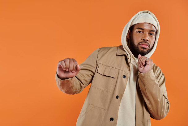 Un hombre afroamericano con una sudadera con capucha que golpea una pose elegante con un telón de fondo vibrante. - Foto, imagen