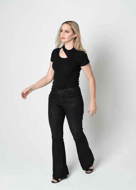 portrét krásné blondýny v moderní černé košili a kožených kalhotách. Sebevědomá stojící póza s gesty ruky, izolované na bílém pozadí studia. - Fotografie, Obrázek