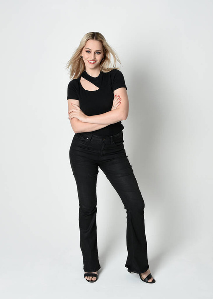 Ganzkörperporträt einer schönen blonden Frau in modernem schwarzen Hemd und Lederhose. Selbstbewusste Stehhaltung mit Handgesten, isoliert auf weißem Studiohintergrund. - Foto, Bild