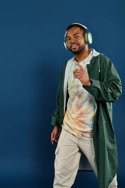 A stylish African American man wearing headphones poses against a vibrant blue backdrop. - Foto, Imagem