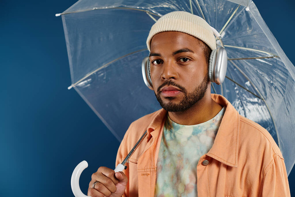 Stylish man with headphones holding umbrella against vibrant backdrop. - Zdjęcie, obraz