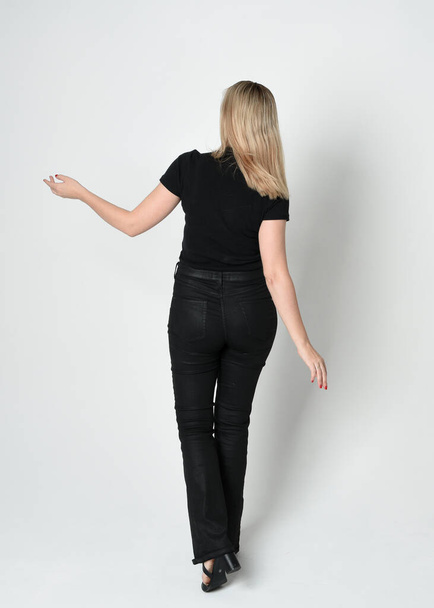 Ganzkörperporträt einer schönen blonden Frau in modernem schwarzen Hemd und Lederhose. Selbstbewusst im Stehen vor der Kamera, Silhouette auf weißem Studiohintergrund. - Foto, Bild