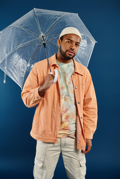 Stylowy Afroamerykanin trzymający nad głową parasol na żywym tle. - Zdjęcie, obraz