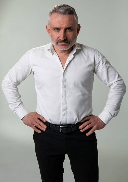 A man in a white dress shirt and black pants is standing confidently with his hands on his hips, showcasing a strong posture and determined gesture - Fotó, kép