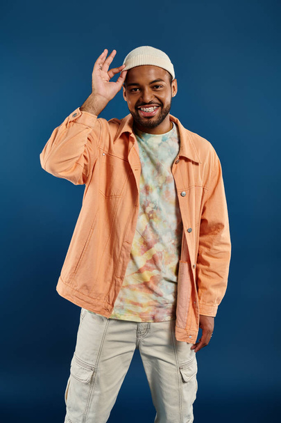 Stijlvolle Afro-Amerikaanse man poserend tegen een levendige achtergrond met oranje jas en witte hoed. - Foto, afbeelding