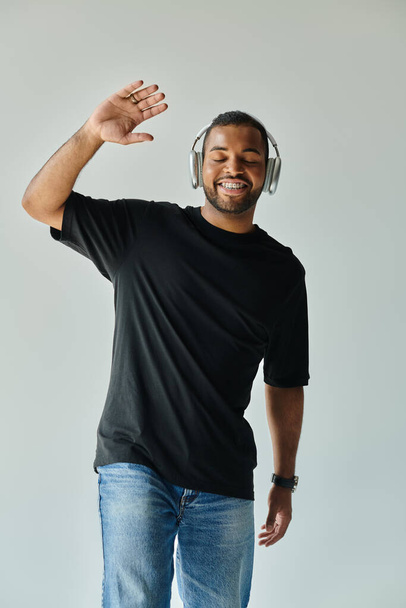 Стильний афроамериканський чоловік, одягнений в навушники і чорну сорочку, позує на яскравий фон. - Фото, зображення