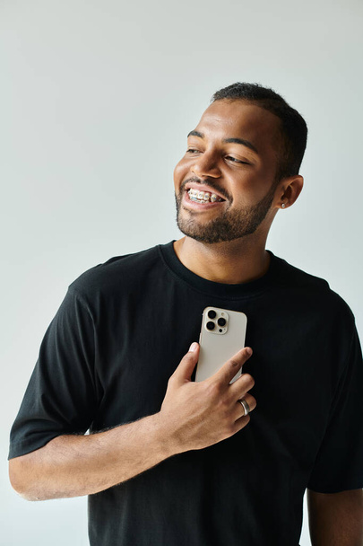 Стильний афроамериканський чоловік сміється, тримаючи мобільний телефон. - Фото, зображення
