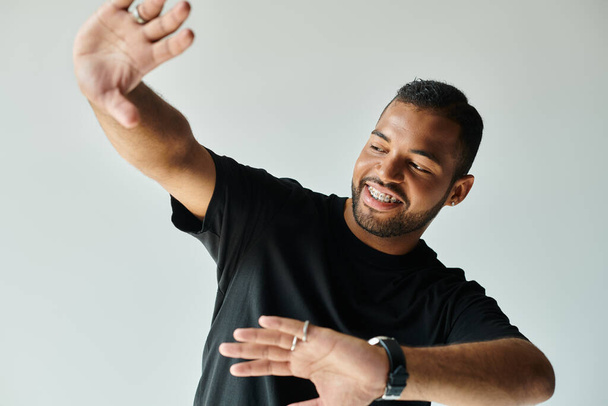 Stilvoller afroamerikanischer Mann hebt anmutig die Hände vor lebendigem Hintergrund. - Foto, Bild
