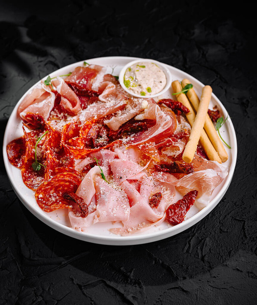 Elegant serving of cured meats with condiments and breadsticks on a dark background - Photo, Image