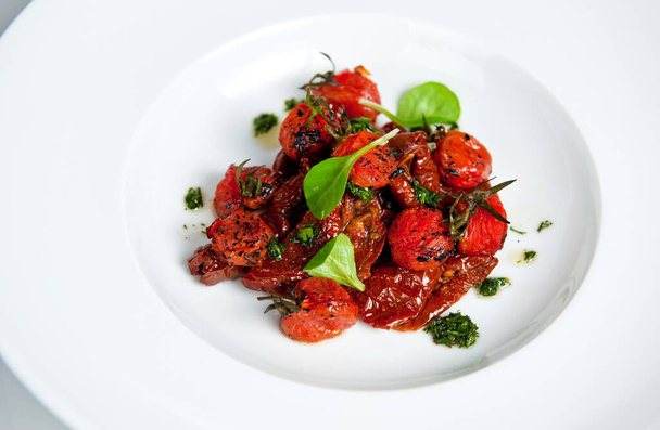 Elegant presentation of seasoned roasted cherry tomatoes with fresh basil on a pristine white dish - Фото, зображення
