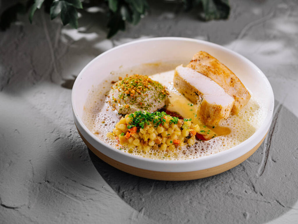 Plate of succulent chicken breast, coupled with spiced couscous and a delicate foam, on a modern table - Foto, Bild
