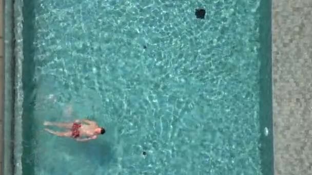 Aerial view of caucasian man swimming on his back in a pool in summer in slow motion - Filmmaterial, Video