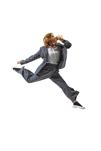 Прыгаю на работу. Молодая женщина в костюме пьет кофе и прыгает в движении на белом фоне студии. Концепция бизнеса, работы и учебы, хобби, фриланса, офиса. Объявление - Фото, изображение
