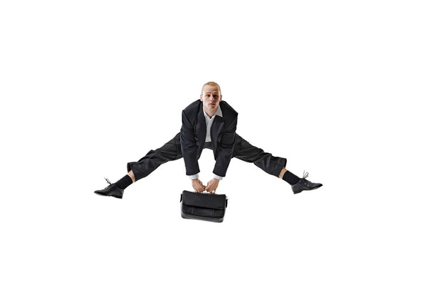 Geschäftsmann beweist beeindruckende Flexibilität, indem er breitbeinige Stretchübungen macht, während er die Aktentasche hält. Dynamische Problemlösung. Geschäfts-, Arbeits- und Studienkonzept, Hobby, Freiberuflichkeit, Büro. Anzeige - Foto, Bild