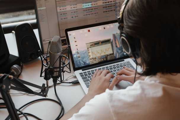 Close-up of an individual using a laptop for audio production, with a professional microphone and headphones. - Foto, Bild