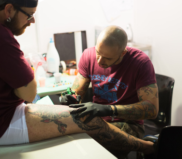 Artist doing tattoo on  client's leg - Foto, imagen