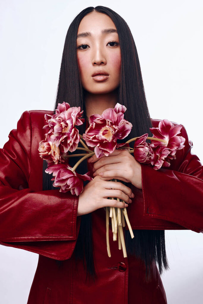 Портрет красивой женщины с длинными черными волосами и красной курткой, держащей букет цветов в саду - Фото, изображение