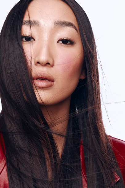 Portret stylowej azjatki z długimi czarnymi włosami i czerwoną kurtką pozującą pewnie do aparatu - Zdjęcie, obraz
