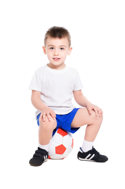 Jongen in voetbal uniforme zittend op bal - Foto, afbeelding
