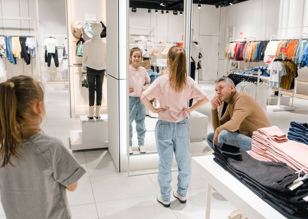 Bir baba ve küçük kızı lüks bir giyim mağazasında moda bir kıyafet denerken bir anı paylaşıyorlar. - Fotoğraf, Görsel