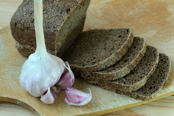 Un pain et de l'ail disposés sur une planche à découper en bois. - Photo, image