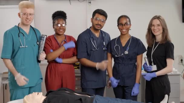 Grupo de médicos de pie junto a la cama con maniquí en el curso de formación de primeros auxilios - Metraje, vídeo