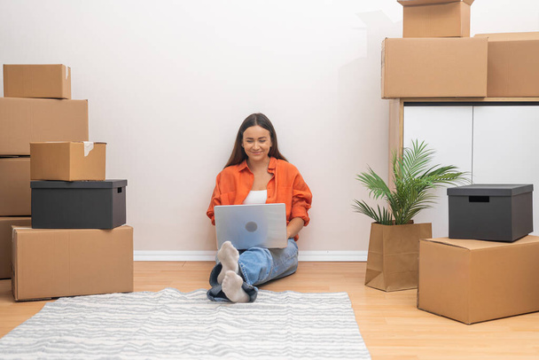 Vonzó nő sötét haj laptoppal élvezi mozgó elegáns lakás nézi a különböző helyszínek új elemek díszítésére belső ház - Fotó, kép