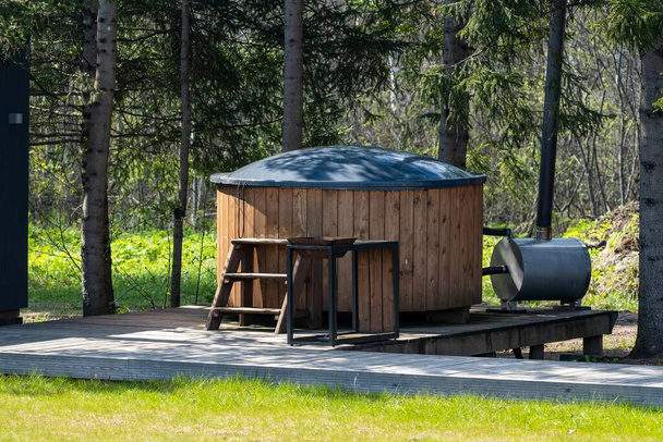 A wooden hot tub with a metal stove in a serene forest setting, perfect for outdoor relaxation and enjoying nature. - Foto, Imagem