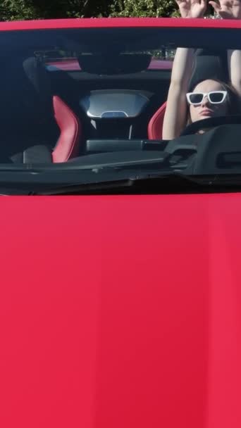 Een meisje zit achter het stuur van een rode auto met haar handen omhoog, geniet van het leven, een rijk leven, veel geld.. Luxe auto en meisje  - Video