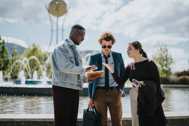 Three mixed race business professionals engaging in a discussion outdoors. They are reviewing data on a tablet, brainstorming solutions, and strategizing for growth. - Photo, Image