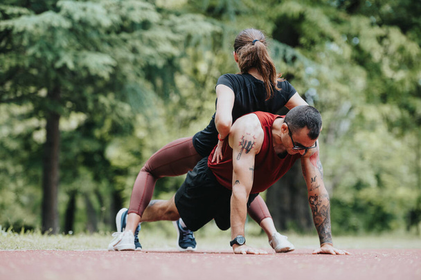 Parkta bir fitness ikilisi yakalayan enerjik bir fotoğraf. Bir kadın, şınav çeken bir erkeğe yardımcı olur.. - Fotoğraf, Görsel