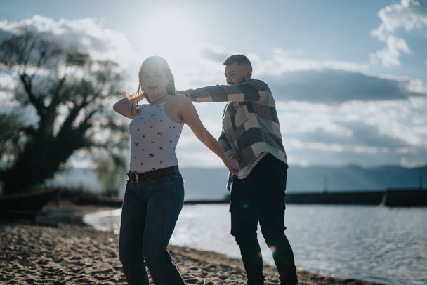 Ένα ευτυχισμένο ζευγάρι απολαμβάνει ένα παιχνιδιάρικο χορό σε μια αμμώδη παραλία, συλλαμβάνοντας την ουσία της χαράς και της συντροφικότητας στο ταξίδι των διακοπών τους. - Φωτογραφία, εικόνα