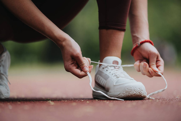 Close-up image showing a focused athlete tying their shoelaces on a red running track, preparing for a workout. - Fotografie, Obrázek