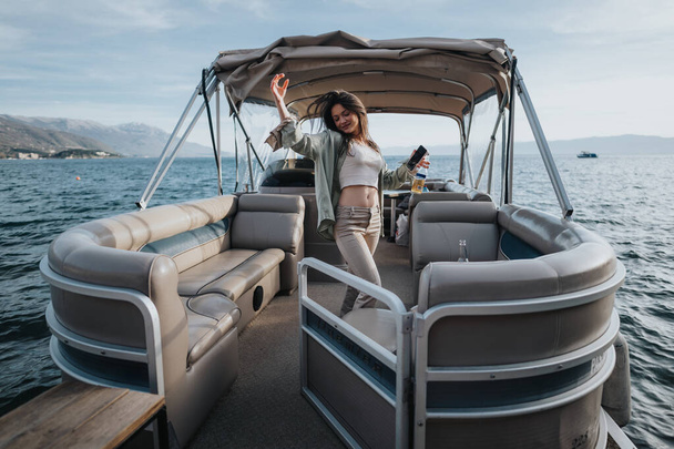 Ein fröhliches, fröhliches Mädchen hebt zur Feier die Arme, während es auf einem Pontonboot steht, umgeben von wunderschönen Berg- und Wasserlandschaften. - Foto, Bild