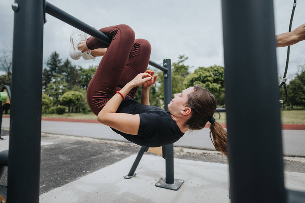 Een fitte jonge vrouw neemt deel aan een uitdagende training met behulp van outdoor fitnessapparatuur in een park, vertonen kracht en behendigheid. - Foto, afbeelding