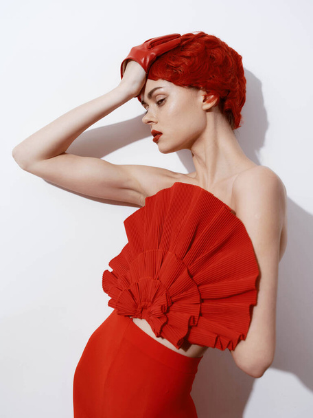 Mulher bonita com vestido vermelho e cabelo posando na frente da parede branca em pose de estilo de moda elegante - Foto, Imagem