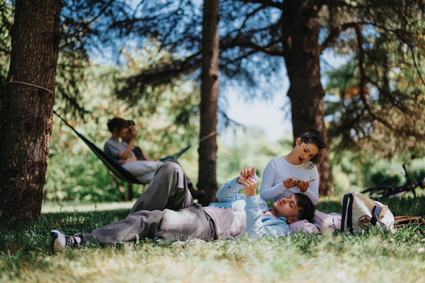 若い友人のグループはリラックスして公園で晴れた日を楽しんで,ピクニックブランケットとハンモックで笑いとレジャーの瞬間を共有します.. - 写真・画像