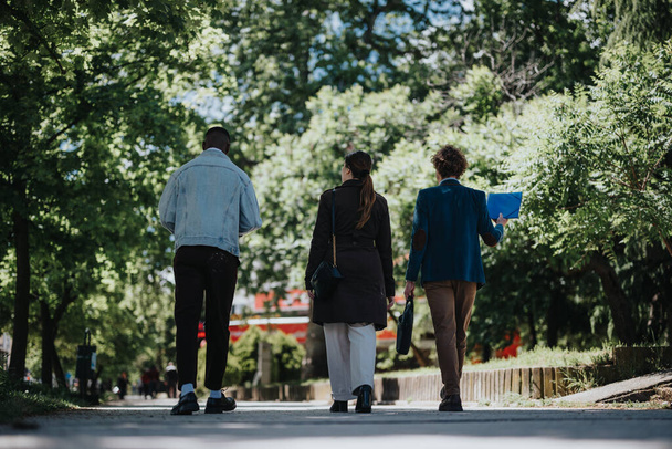 Üç çok kültürlü iş adamı verimli bir şehir parkında yürürken, takım çalışmasını ve işbirliğini sembolize eden bir proje hakkında ciddi bir tartışmaya giriştiler.. - Fotoğraf, Görsel