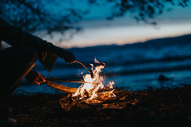 湖の近くのキャンプファイヤーを楽しむ友人の居心地の良い夜のシーン 火の上の食べ物を焙煎しながら,トータルな瞬間 - 写真・画像
