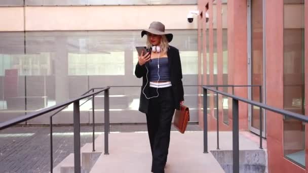 Satisfied with the results, the businesswoman walking down the street outside the office building, a boss holds a phone in her hands, writes messages and reads news online, using an app. - Felvétel, videó