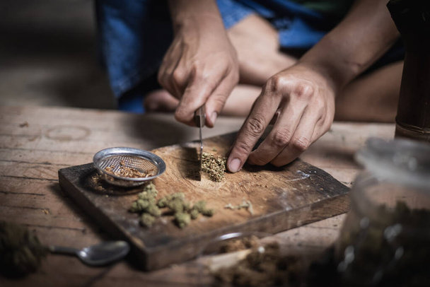 A man prepares marijuana on a cutting board to smoke, person who smokes drugs, drug addict, Drugs addiction and withdrawal symptoms concept. drugsInternational Day against Drug Abuse. - Фото, изображение