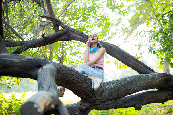 Alone Woman talking on phone while sitting on tree branch - Φωτογραφία, εικόνα