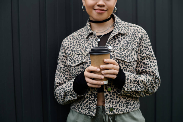 Una joven vestida con estilo sosteniendo una taza de café frente a una elegante pared negra. - Foto, imagen