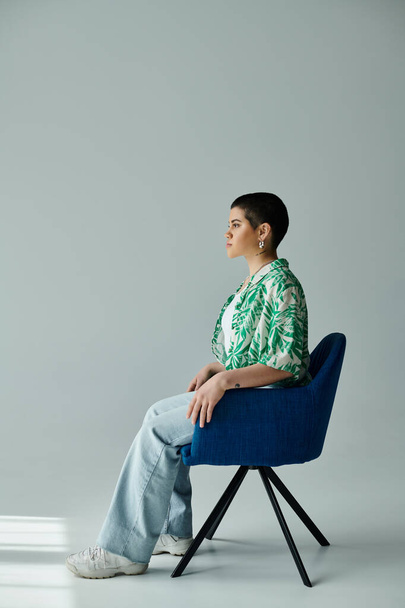 Una joven con el pelo corto se sienta en una silla azul, en una pose serena. - Foto, Imagen