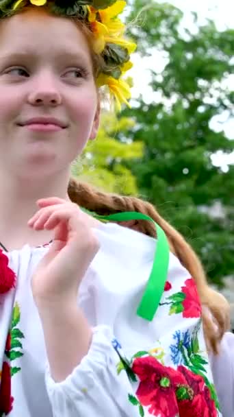 επικοινωνία των δύο νέων όμορφα κορίτσια στην ουκρανική εθνικά φορέματα πλέξιμο πλεξούδες στέκεται με στεφάνια στα χέρια τους βάζοντας ένα όμορφο στεφάνι στο κεφάλι ηλιοτρόπια λουλούδια δάσος. κεντήματα - Πλάνα, βίντεο