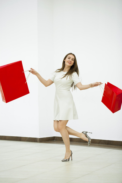 Happy woman holding two red shopping bags walking in the shop - Photo, Image
