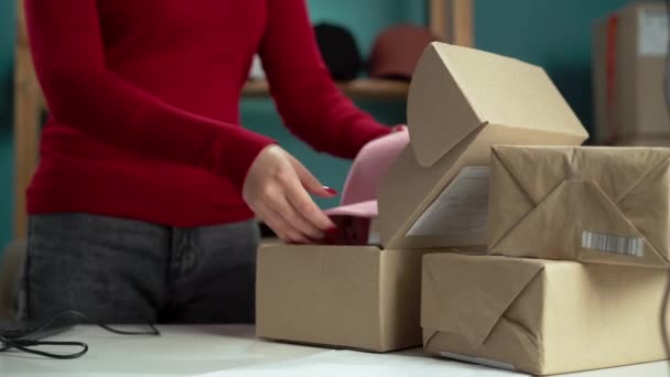 Uma pessoa está preparando caixas de papelão para o transporte, organizando itens e recebendo um chapéu rosa pronto para entrega - Filmagem, Vídeo